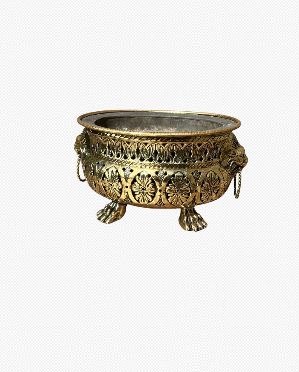 An antique oval pierced brass jardiniere featuring floral repousse panels, lion mask handles with drop rings, and claw feet.