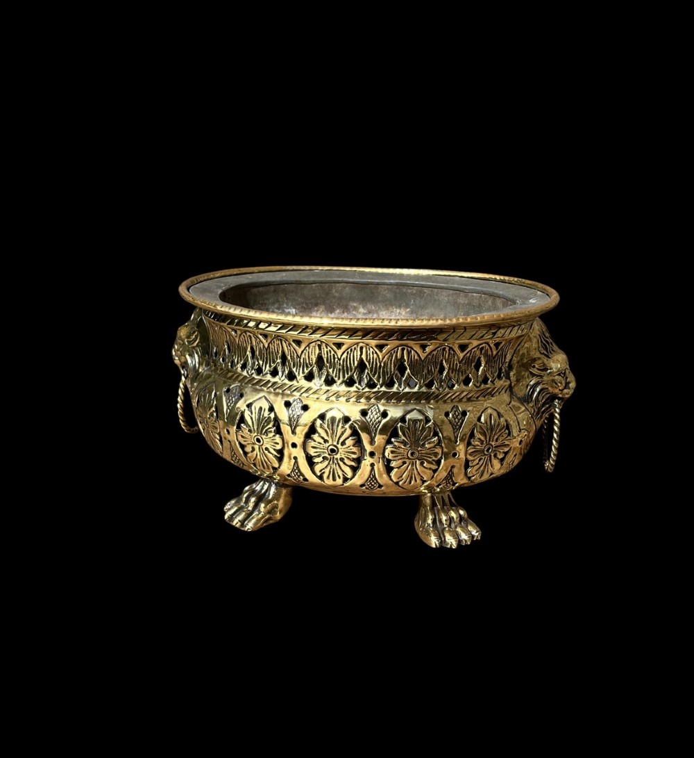 An antique oval pierced brass jardiniere featuring floral repousse panels, lion mask handles with drop rings, and claw feet. View II