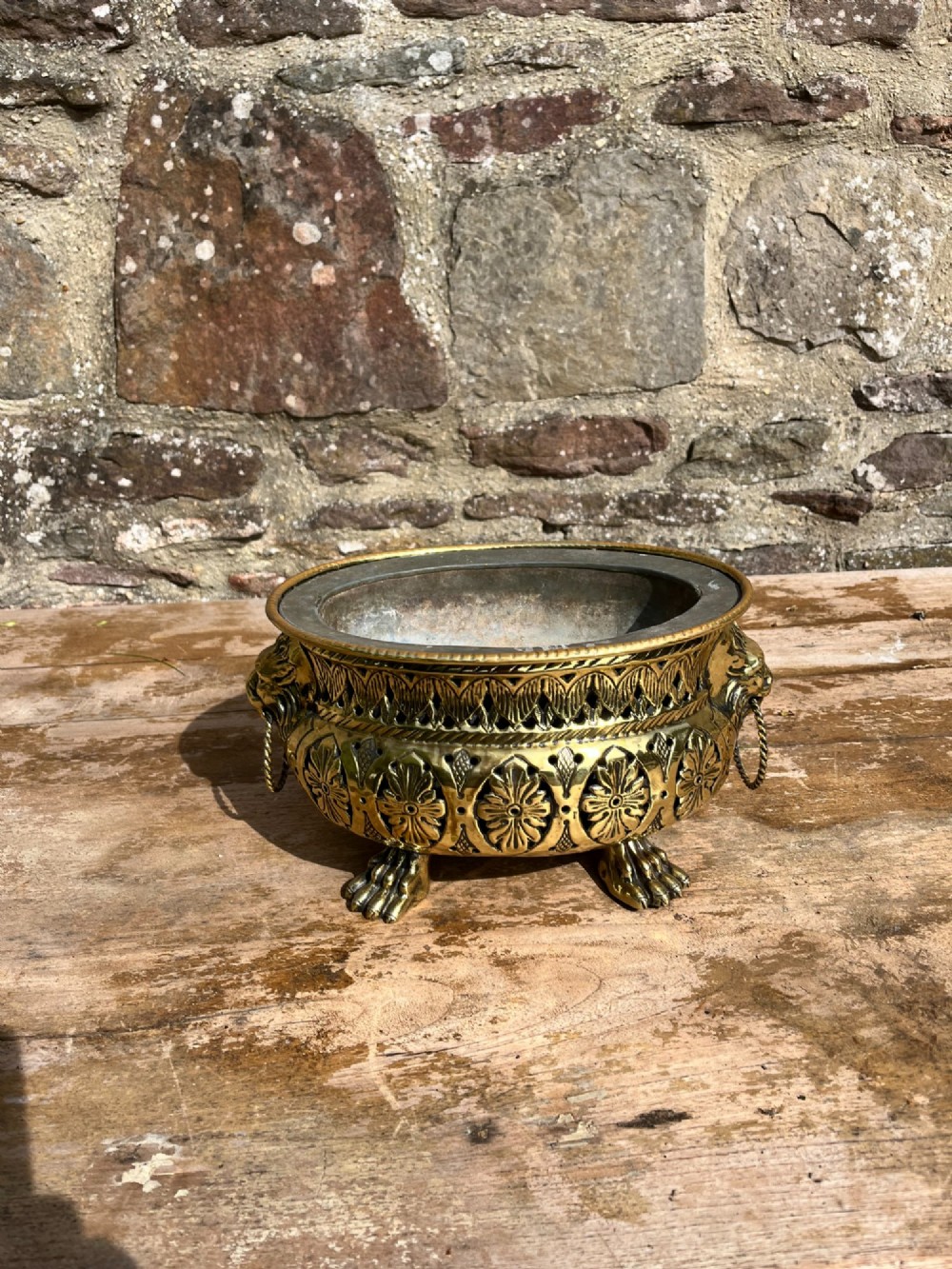 An antique oval pierced brass jardiniere featuring floral repousse panels, lion mask handles with drop rings, and claw feet. View III