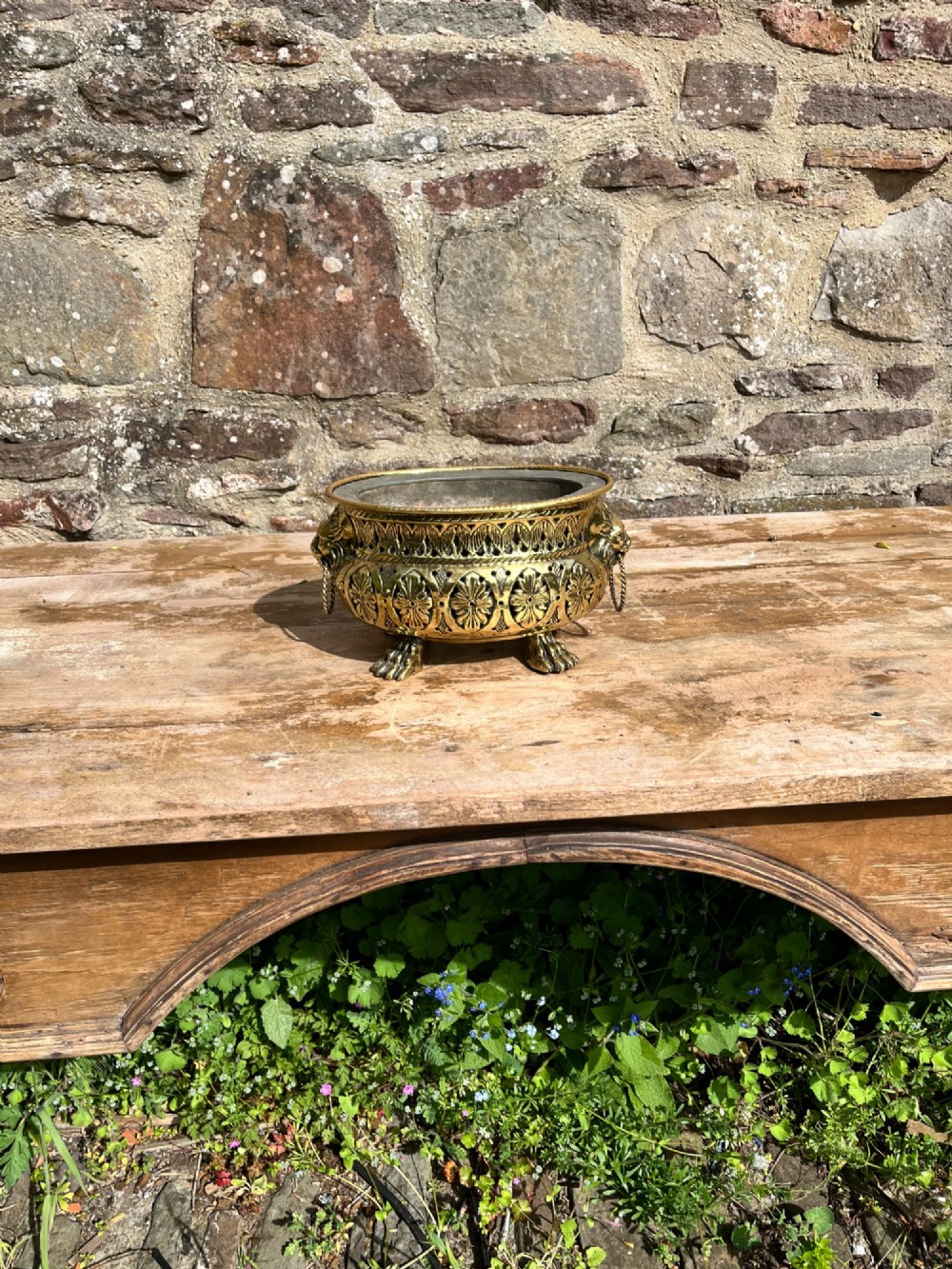 An antique oval pierced brass jardiniere featuring floral repousse panels, lion mask handles with drop rings, and claw feet. View V