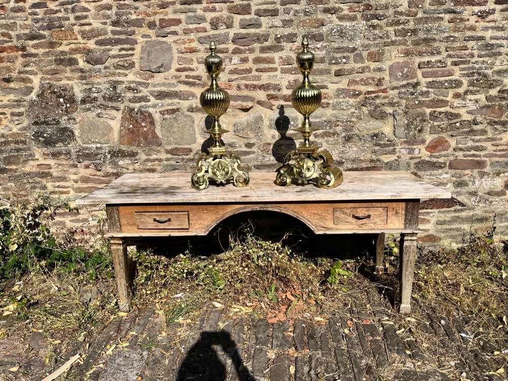 A pair of decorative polished brass French fire dogs with urn finials, gadrooned details, scrolled bases, and central fleur-de-lis motifs. View II
