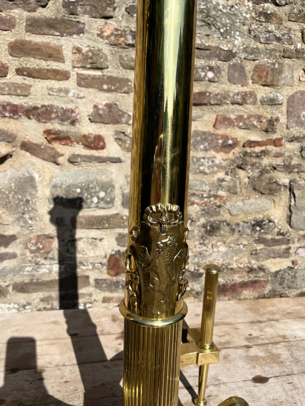 A pair of tall polished brass fire dogs featuring fluted Corinthian columns with relief crests and cabriole legs ending in claw feet. View IV