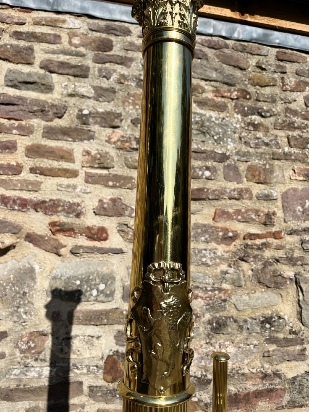 A pair of tall polished brass fire dogs featuring fluted Corinthian columns with relief crests and cabriole legs ending in claw feet. View V