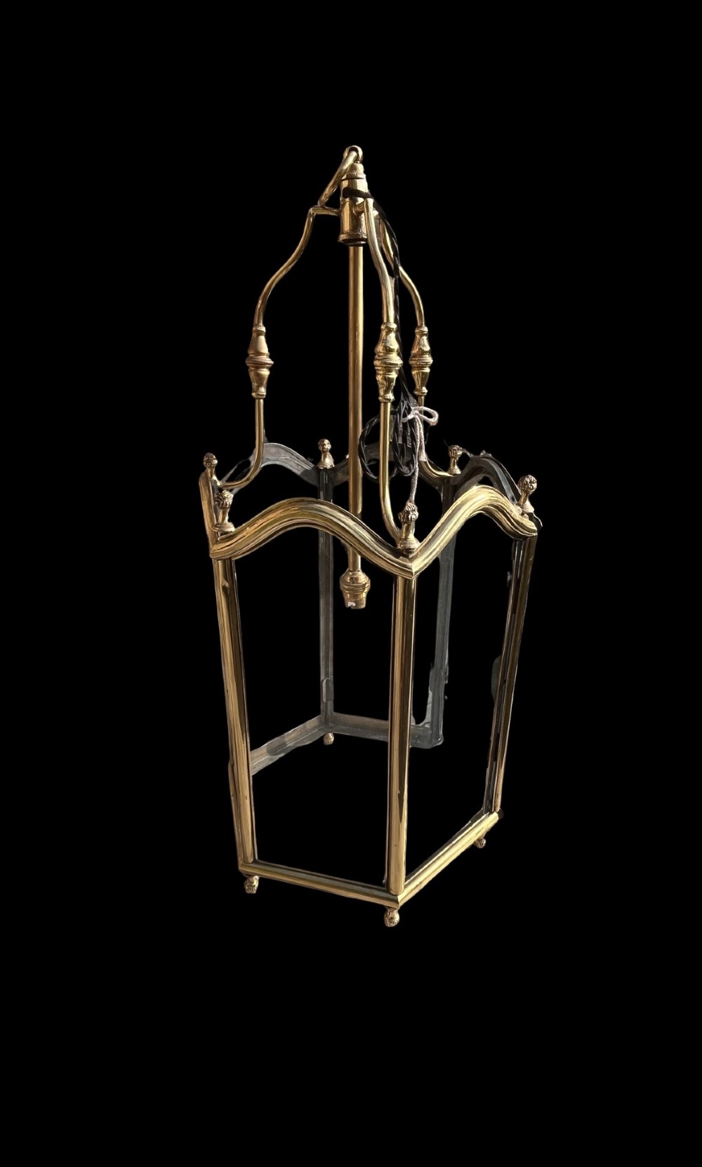 A Victorian brass hall lantern featuring a shaped frame, clear glass side panels, decorative finials, and an upper suspension loop. View II
