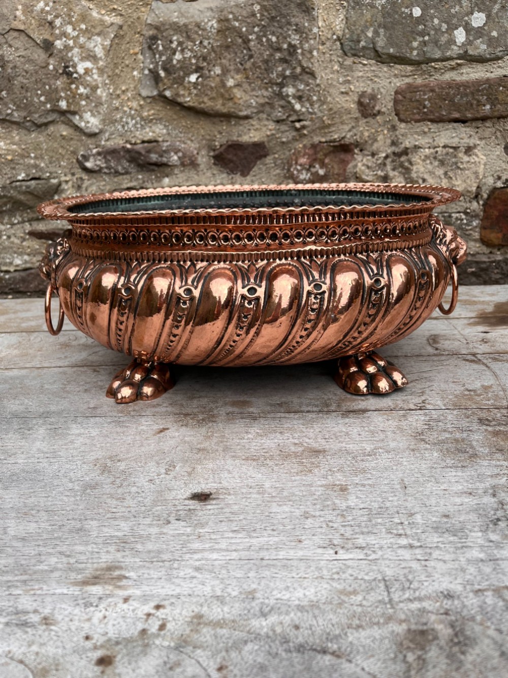 An oval antique copper jardiniere featuring gadrooned body panels, lion mask drop-ring handles, and cast paw feet. View III