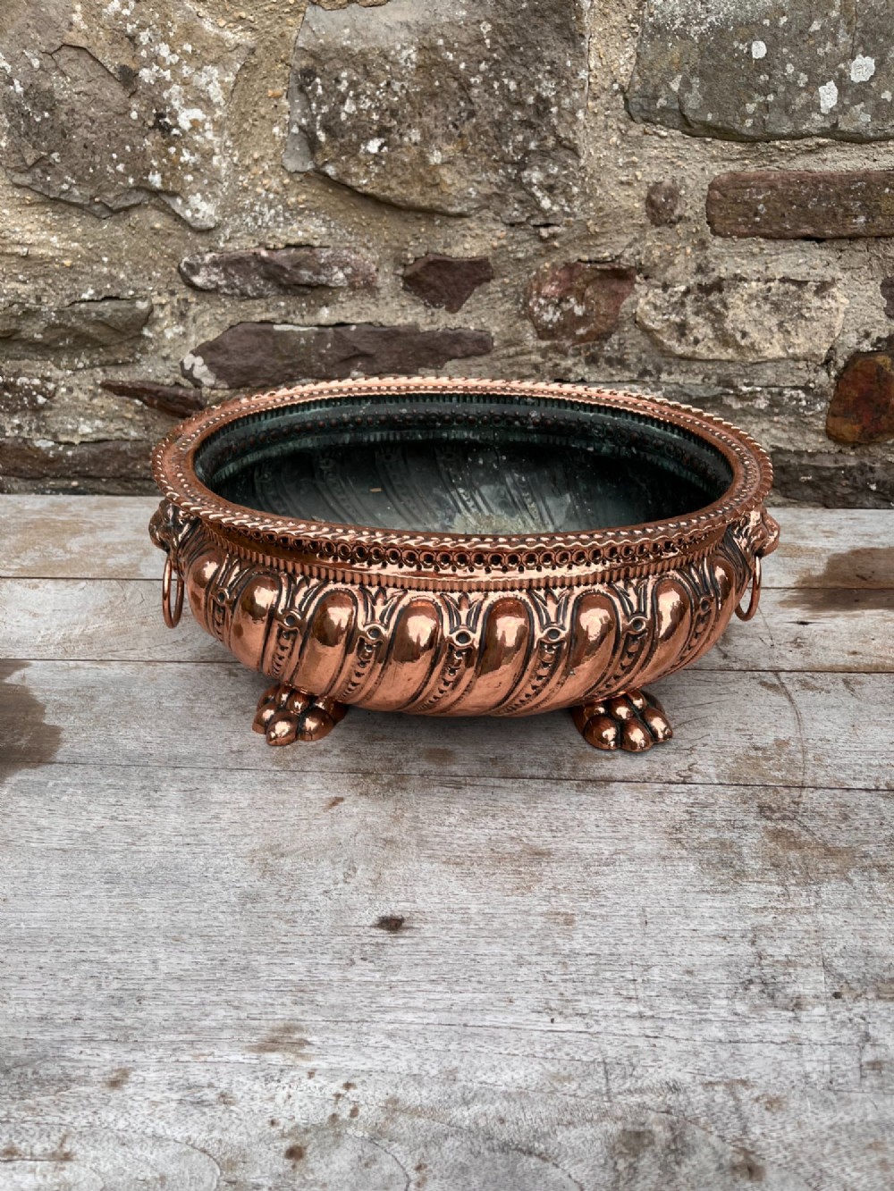 An oval antique copper jardiniere featuring gadrooned body panels, lion mask drop-ring handles, and cast paw feet. View IV