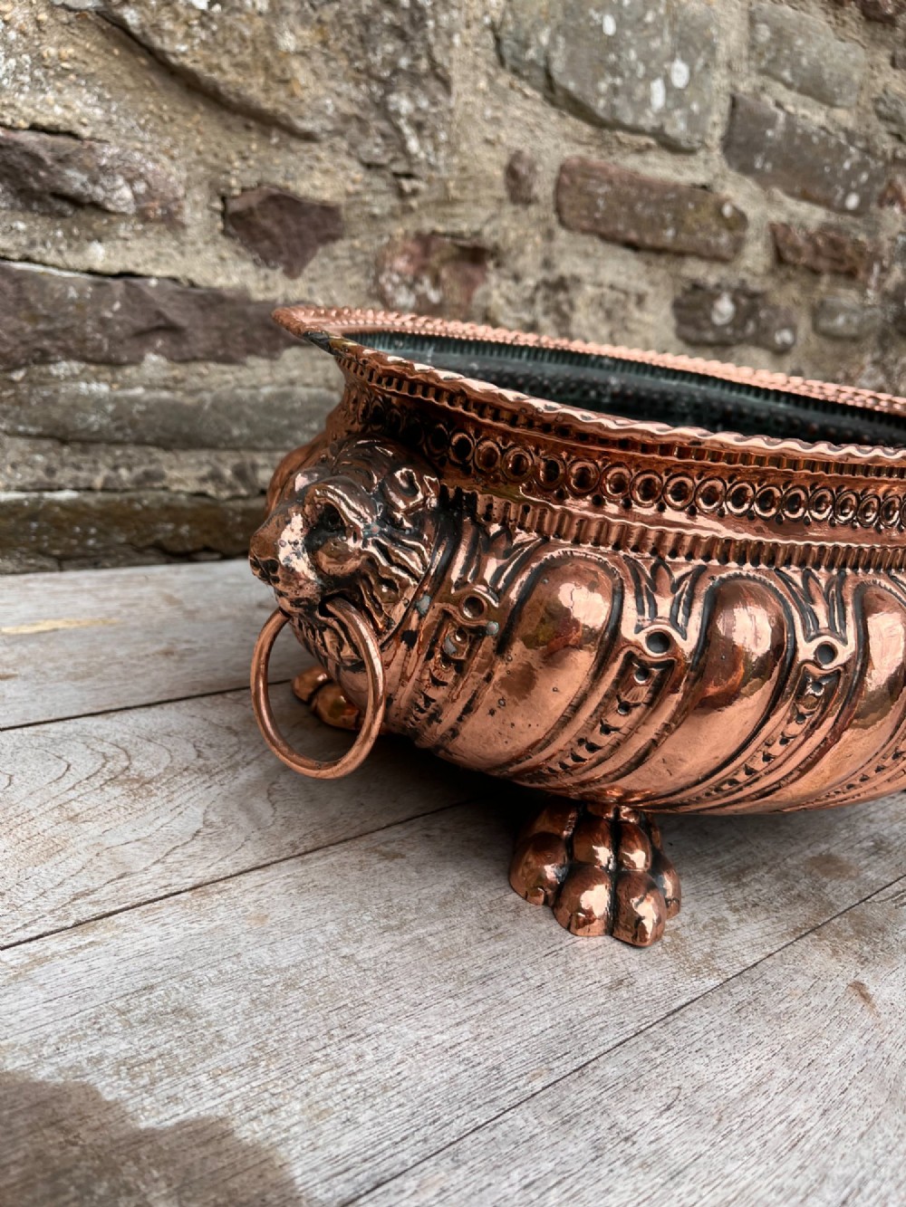 An oval antique copper jardiniere featuring gadrooned body panels, lion mask drop-ring handles, and cast paw feet. View V