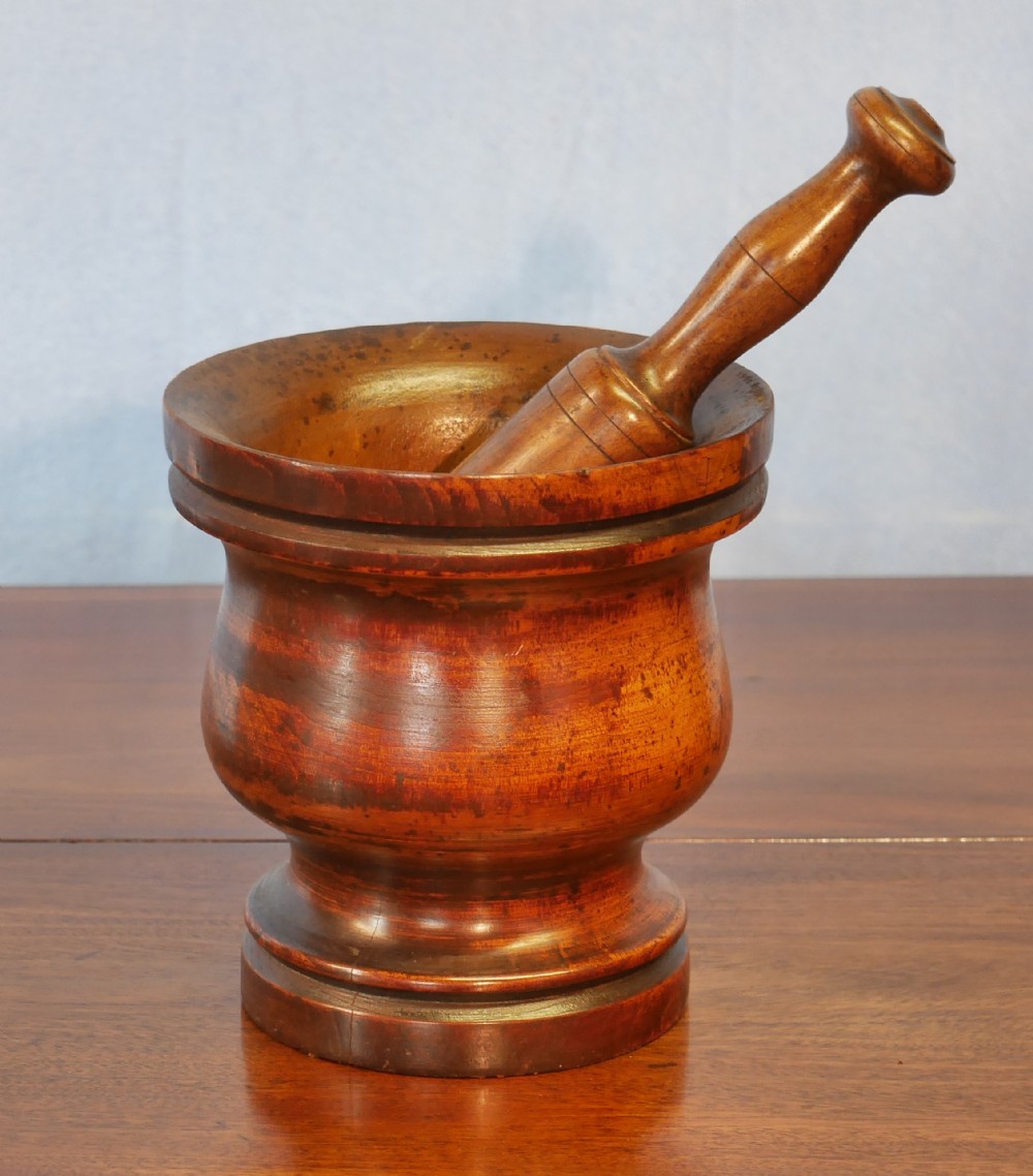 A turned walnut treen mortar with a moulded rim and base, accompanied by a matching turned wooden pestle.