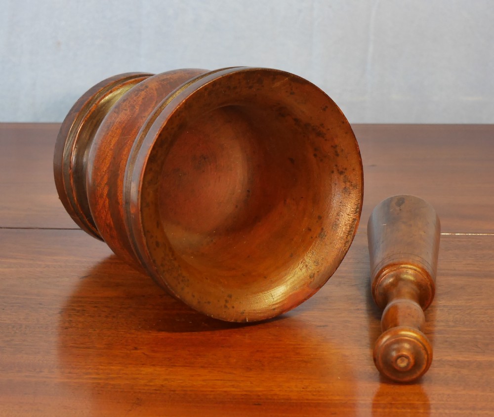 A turned walnut treen mortar with a moulded rim and base, accompanied by a matching turned wooden pestle. View IV