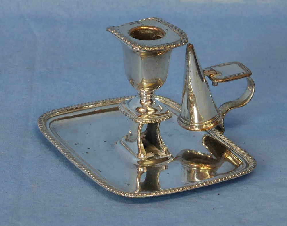 An antique silver-plated chamber candlestick featuring a rectangular tray with gadrooned edges, a central sconce, a side handle, and a removable conical snuffer.