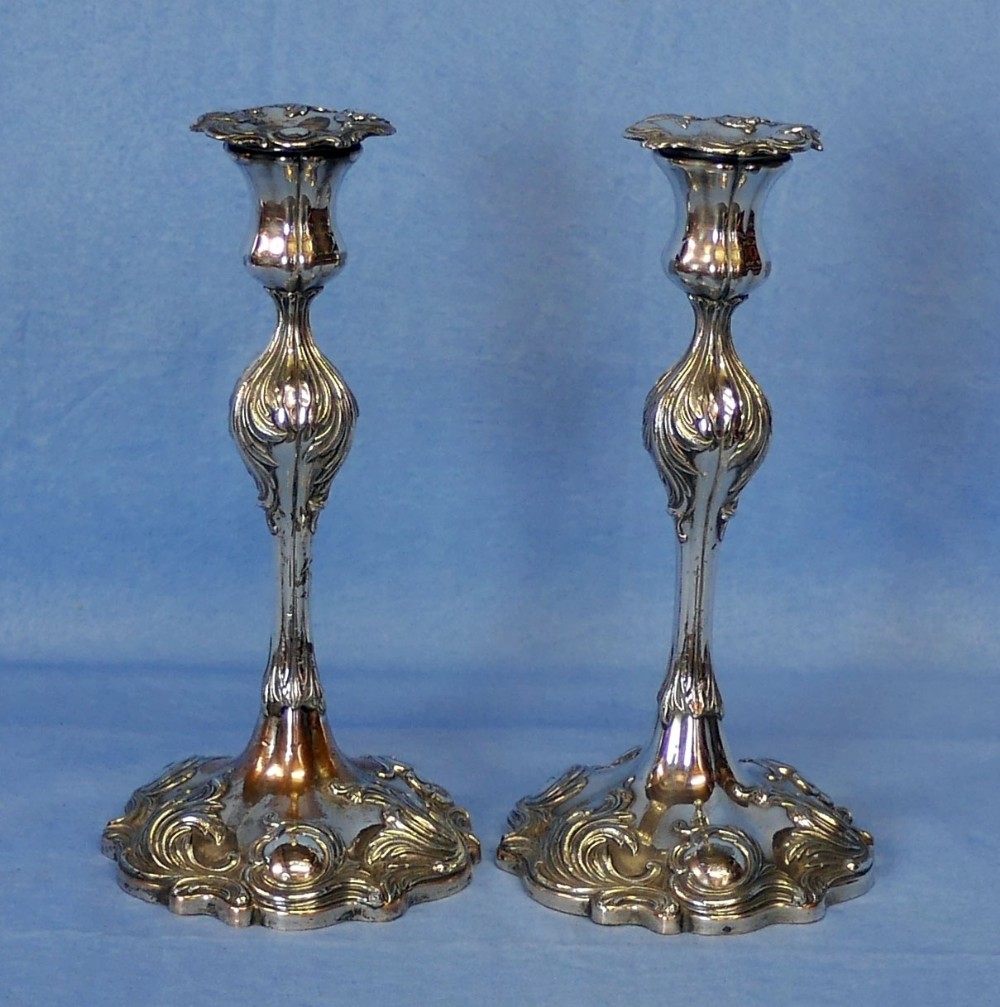 A pair of silver-plated candlesticks decorated with Rococo relief scrollwork on the stems and contoured bases.