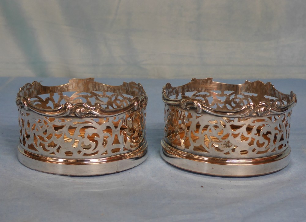 A pair of circular silver-plated wine coasters featuring pierced scrollwork sides and turned wooden bases. View II