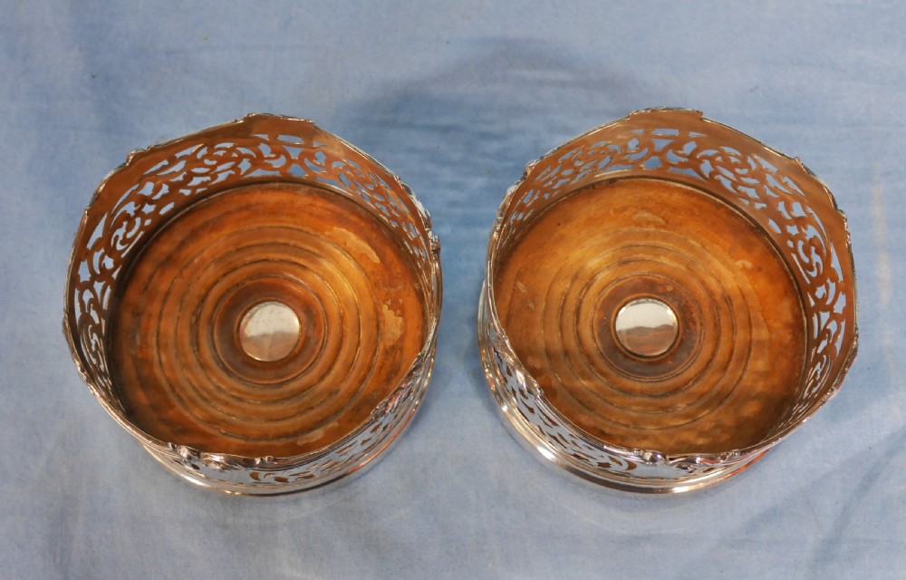 A pair of circular silver-plated wine coasters featuring pierced scrollwork sides and turned wooden bases. View IV