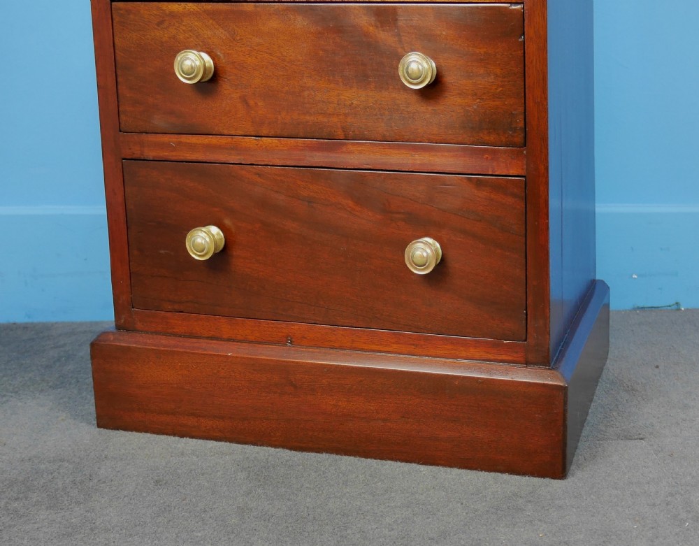 A small mahogany chest of drawers featuring four stacked drawers fitted with turned brass knobs, set on a straight plinth base. View V
