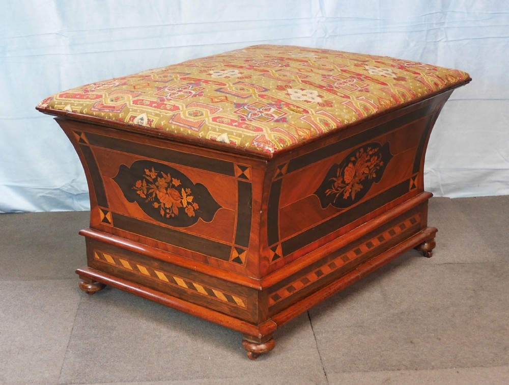 A Victorian walnut storage ottoman featuring concave sides with floral marquetry panels, geometric crossbanding, and a cushioned geometric upholstered top.