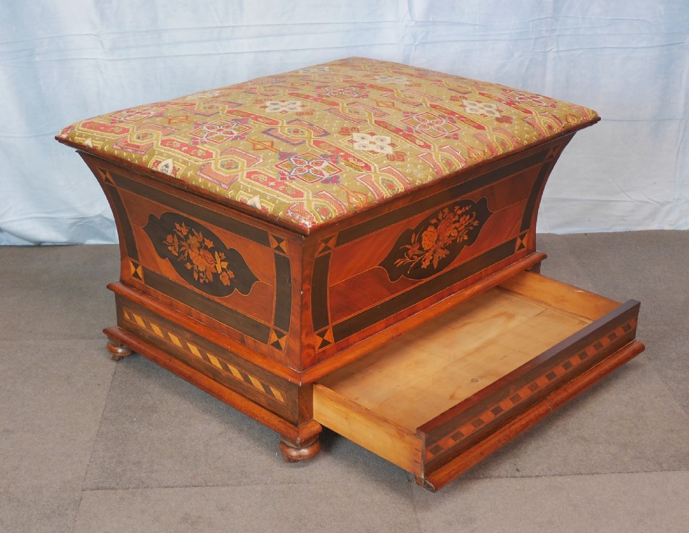 A Victorian walnut storage ottoman featuring concave sides with floral marquetry panels, geometric crossbanding, and a cushioned geometric upholstered top. View II