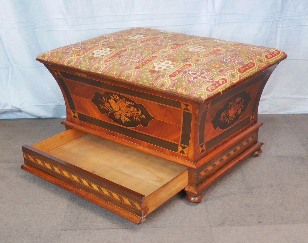 A Victorian walnut storage ottoman featuring concave sides with floral marquetry panels, geometric crossbanding, and a cushioned geometric upholstered top. View III