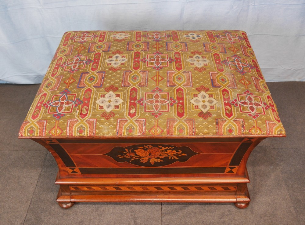 A Victorian walnut storage ottoman featuring concave sides with floral marquetry panels, geometric crossbanding, and a cushioned geometric upholstered top. View VIII