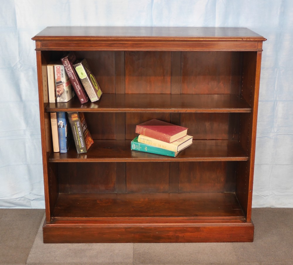 An Edwardian open mahogany bookcase featuring two adjustable shelves, a panelled back, and a solid plinth base.