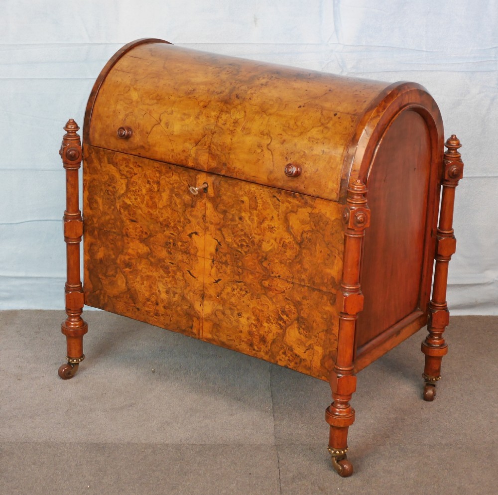 A Victorian burr walnut music canterbury featuring a rounded barrel lid, book-matched veneer panels, turned corner columns, and brass castors. View V