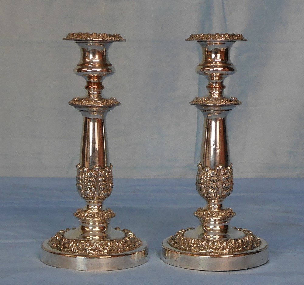 A pair of polished silver-plated candlesticks featuring decorative acanthus leaf foliage moulding on the lower stems and circular bases.