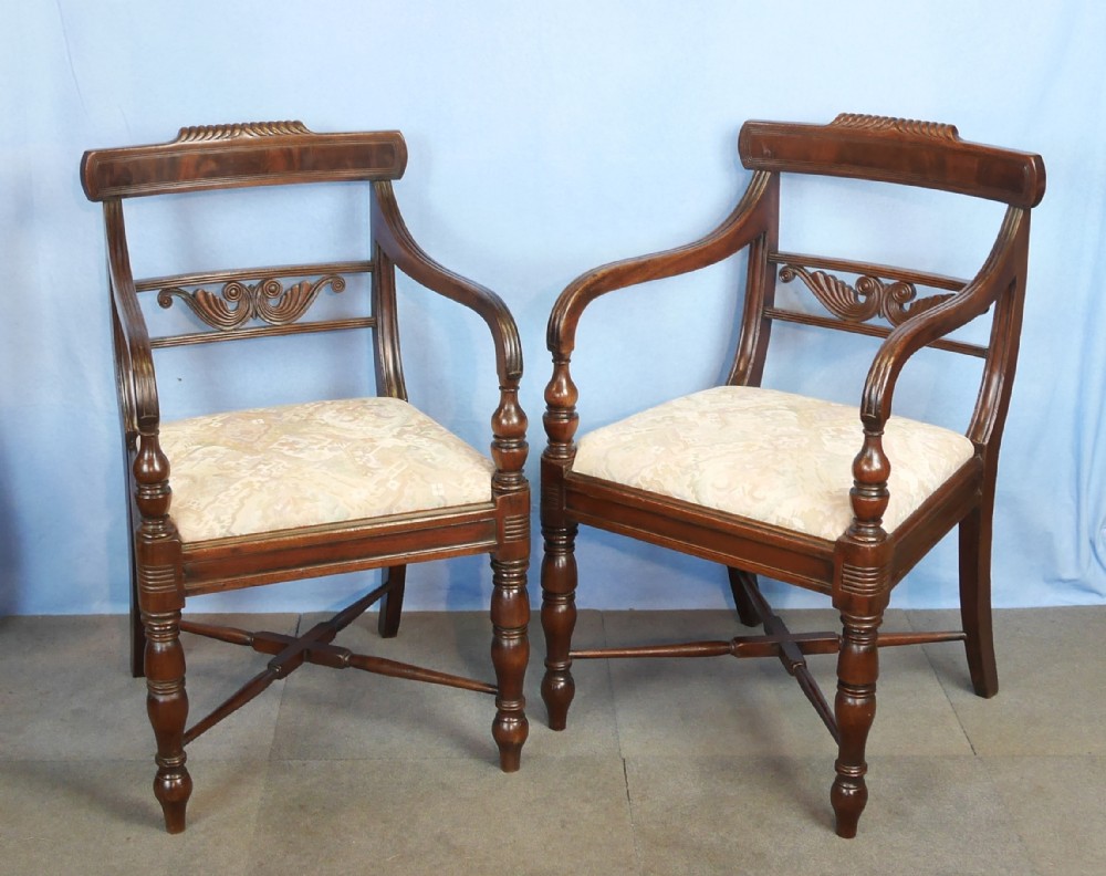 A pair of mahogany Regency style dining armchairs featuring carved backrests, sweeping armrests, turned front legs, and pattern upholstered seats.