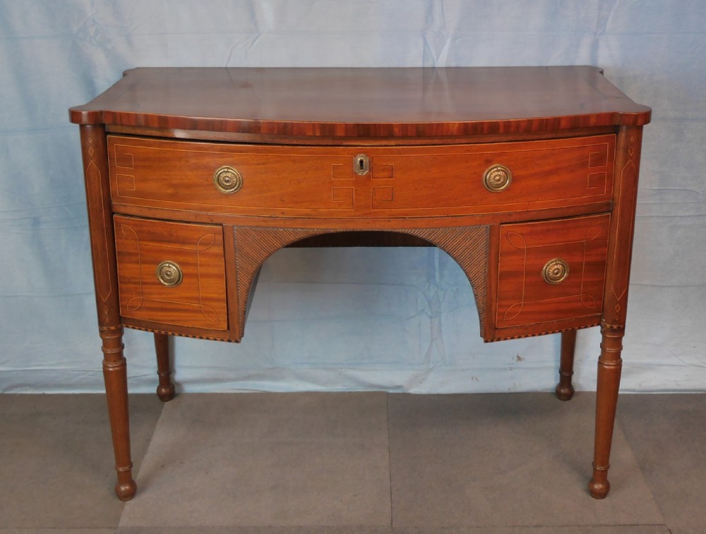 An antique Regency mahogany dressing table featuring a curved front, boxwood stringing inlay, three drawers with brass ring handles, and turned legs.