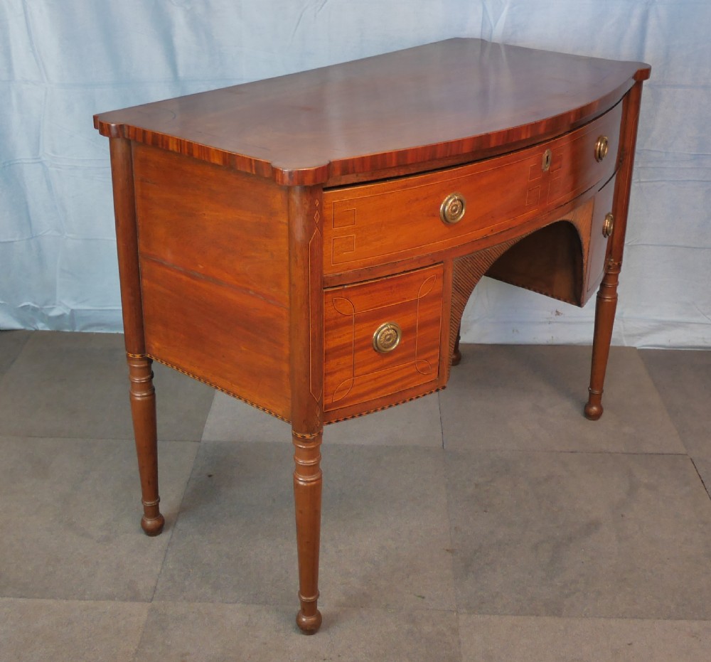 An antique Regency mahogany dressing table featuring a curved front, boxwood stringing inlay, three drawers with brass ring handles, and turned legs. View III