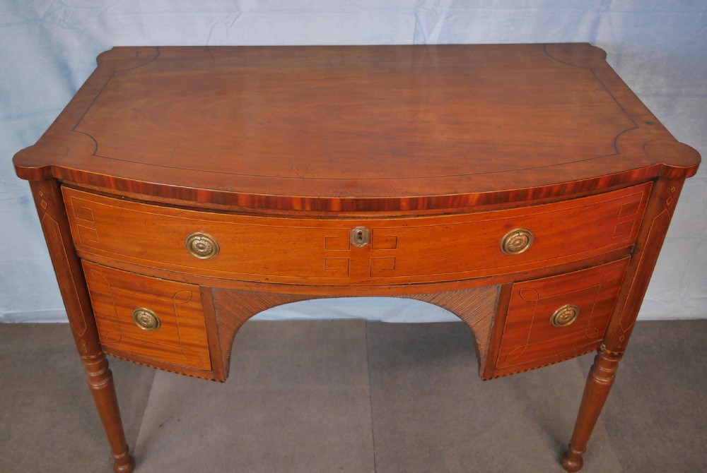 An antique Regency mahogany dressing table featuring a curved front, boxwood stringing inlay, three drawers with brass ring handles, and turned legs. View VI