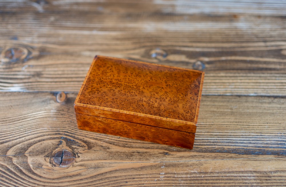 A small rectangular antique box crafted from warm brown amboyna burr wood with fine inlaid line edging.