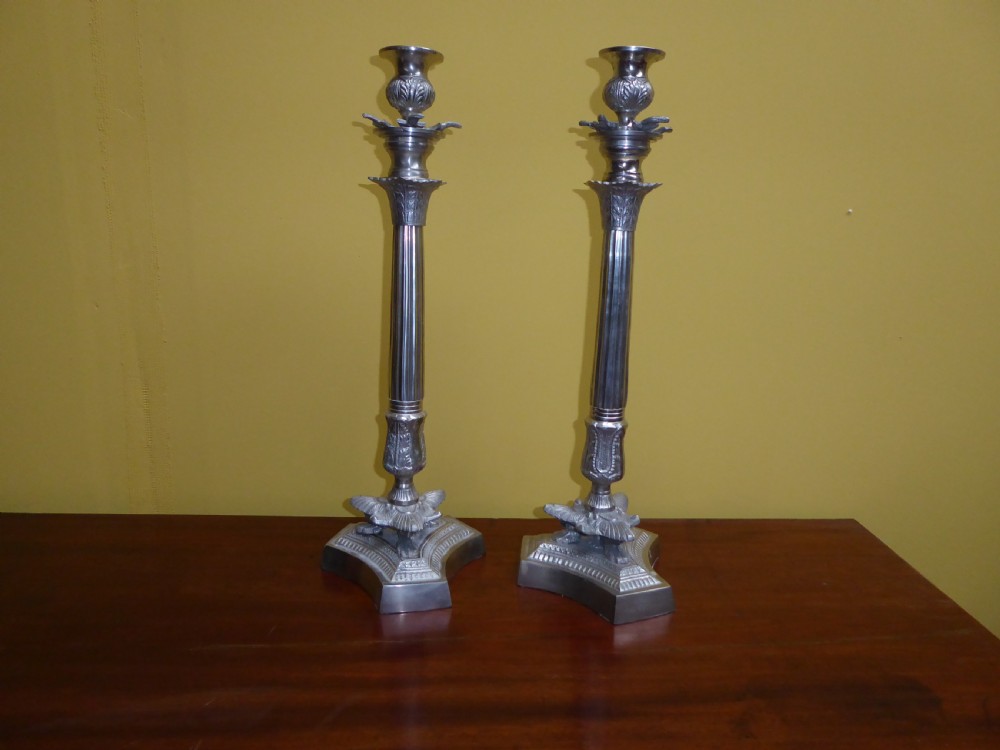 A pair of tall 19th-century silvered metal candlesticks featuring fluted central columns and ornate leaf-embellished tri-form bases. View II