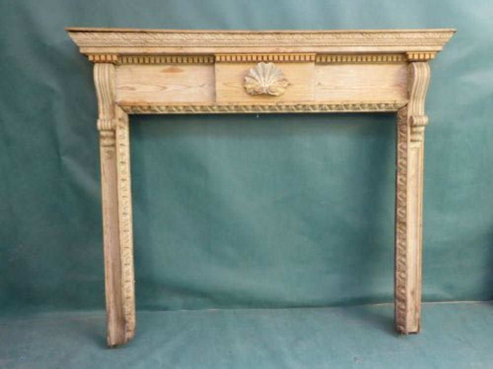 A carved wooden fireplace surround made from pine featuring a central shell carving and dentil moulding along the mantel shelf.