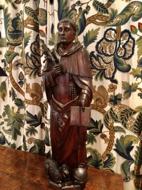 fig 1. A dark carved oak sculpture of a religious figure holding a palm frond and open book with a carved animal at the base.
