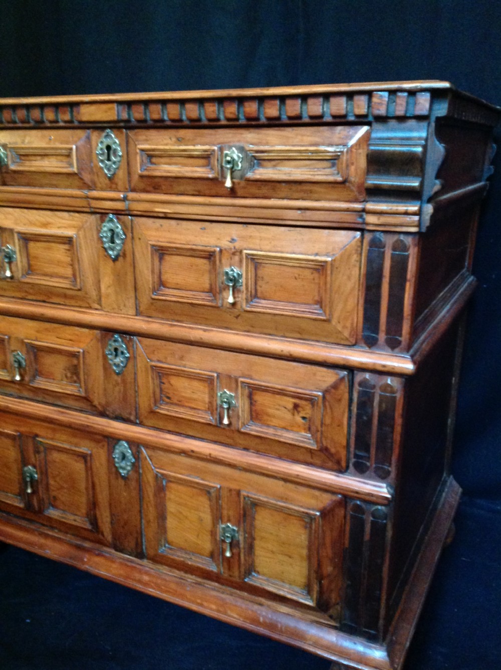 A seventeenth-century cedar chest of drawers featuring geometric moulded drawer fronts, brass drop handles, ornate escutcheons, and bun feet. View VIII