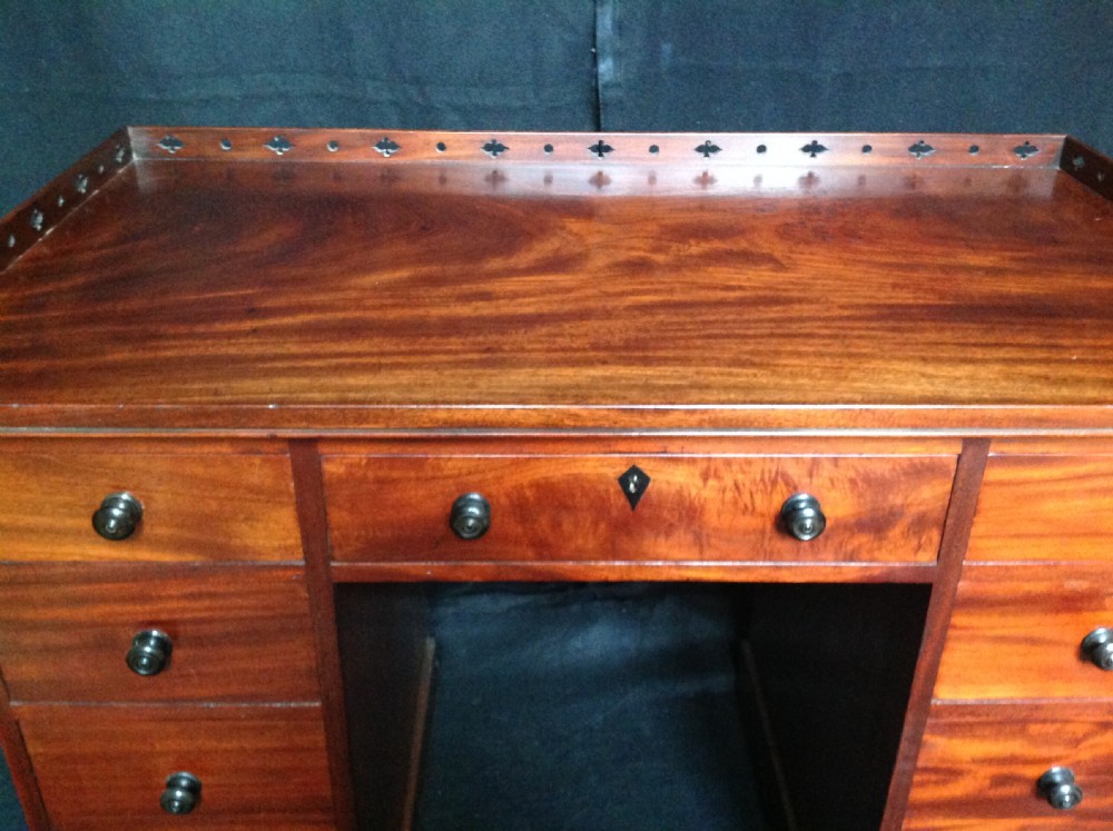 An early 19th-century mahogany pedestal desk featuring nine drawers with turned knobs, a central kneehole, and a pierced gallery back. View V