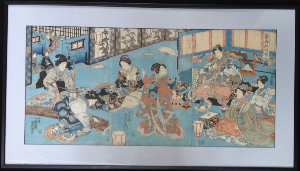 A framed Japanese ukiyo-e triptych woodblock print by Utagawa Kunisada depicting figures inside a traditional domestic setting.