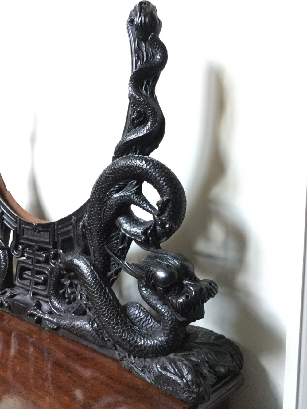 A circular brass plate set within an intricately carved dark wood frame featuring twin dragon motifs on a flat base. View VI