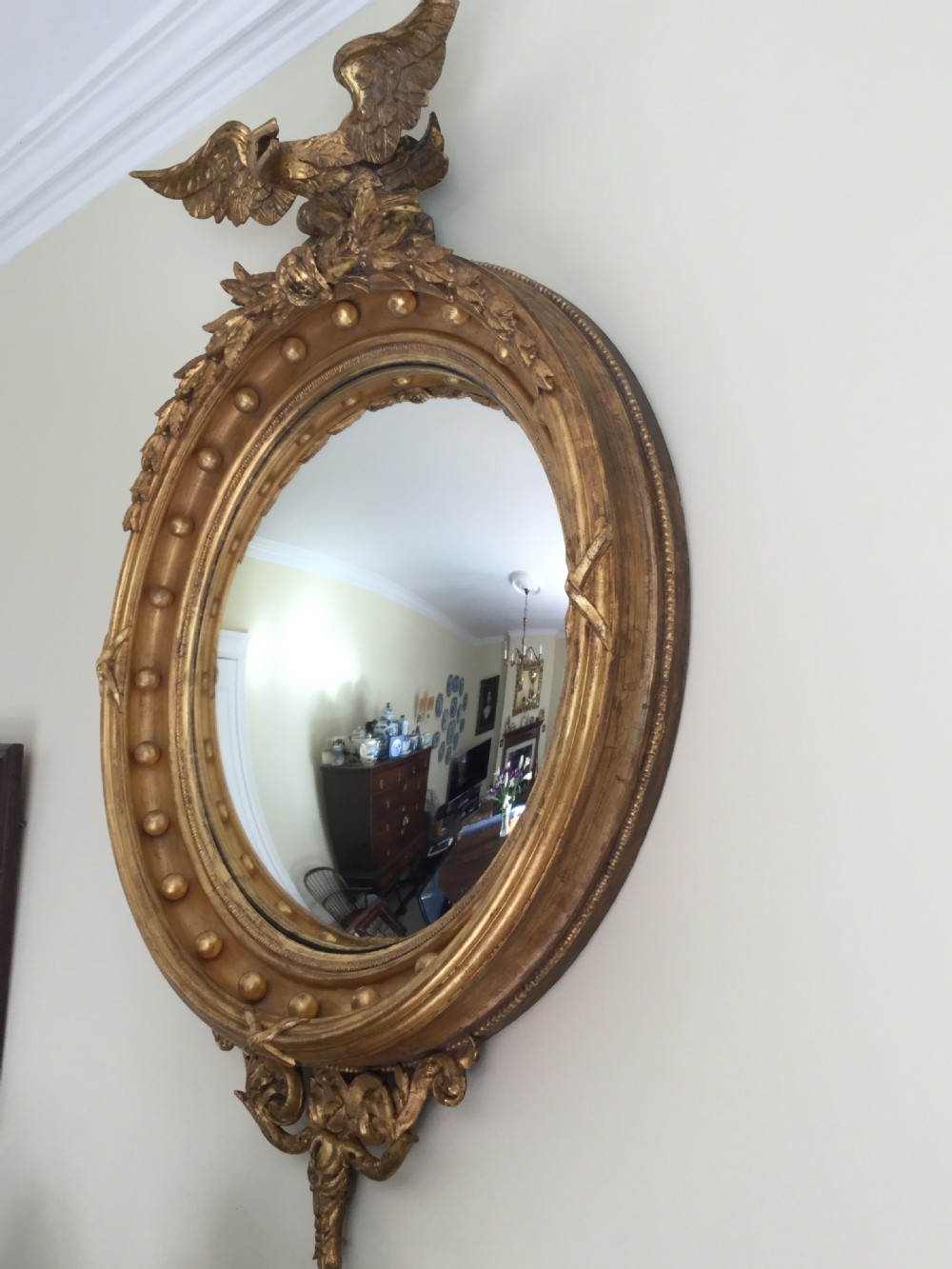 A circular gilded convex wall mirror topped with a carved eagle cresting and decorated with perimeter spherules. View V