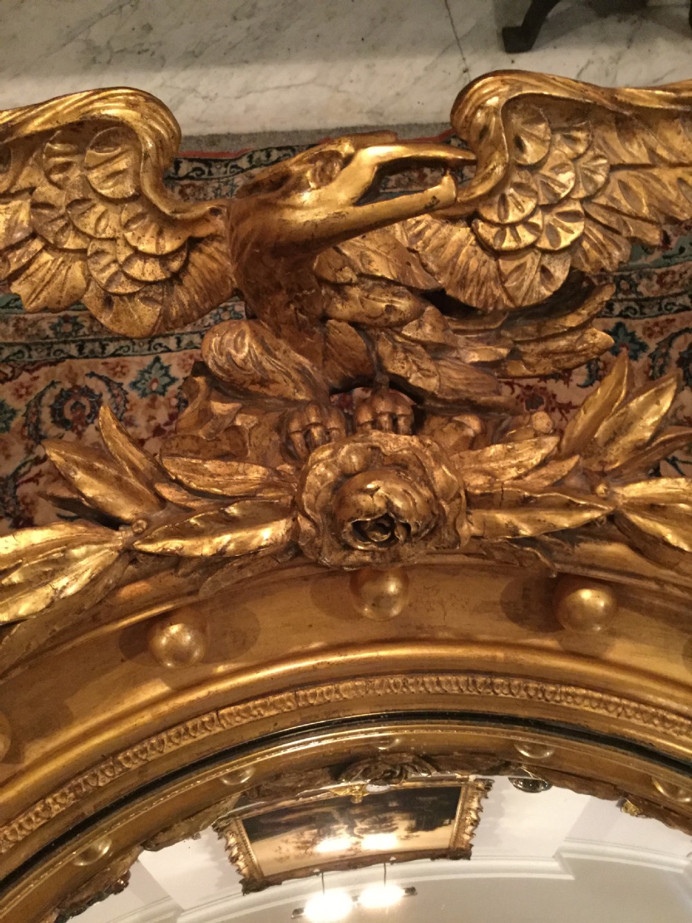 A circular gilded convex wall mirror topped with a carved eagle cresting and decorated with perimeter spherules. View XII