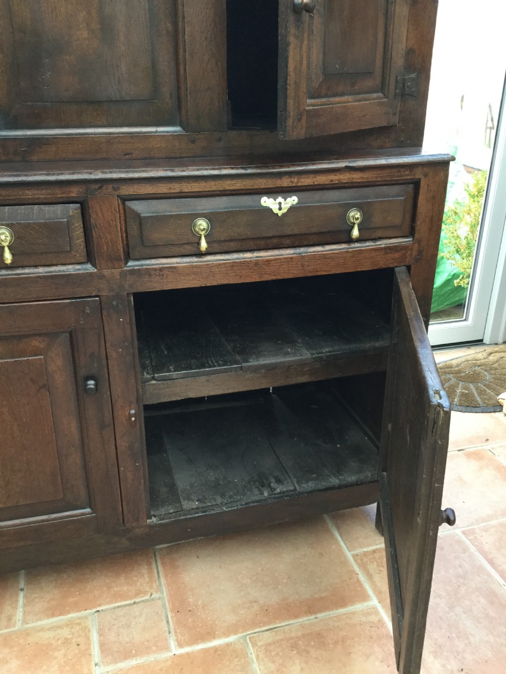 A dark oak 17th-century court cupboard with geometric fielded panelling, carved frieze, pendant drops, two drawers, and double lower doors. View III