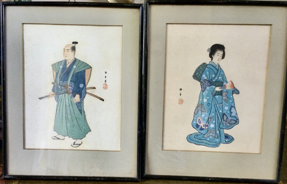 A pair of framed Japanese watercolour paintings depicting a standing samurai with swords and a woman in a patterned blue kimono.