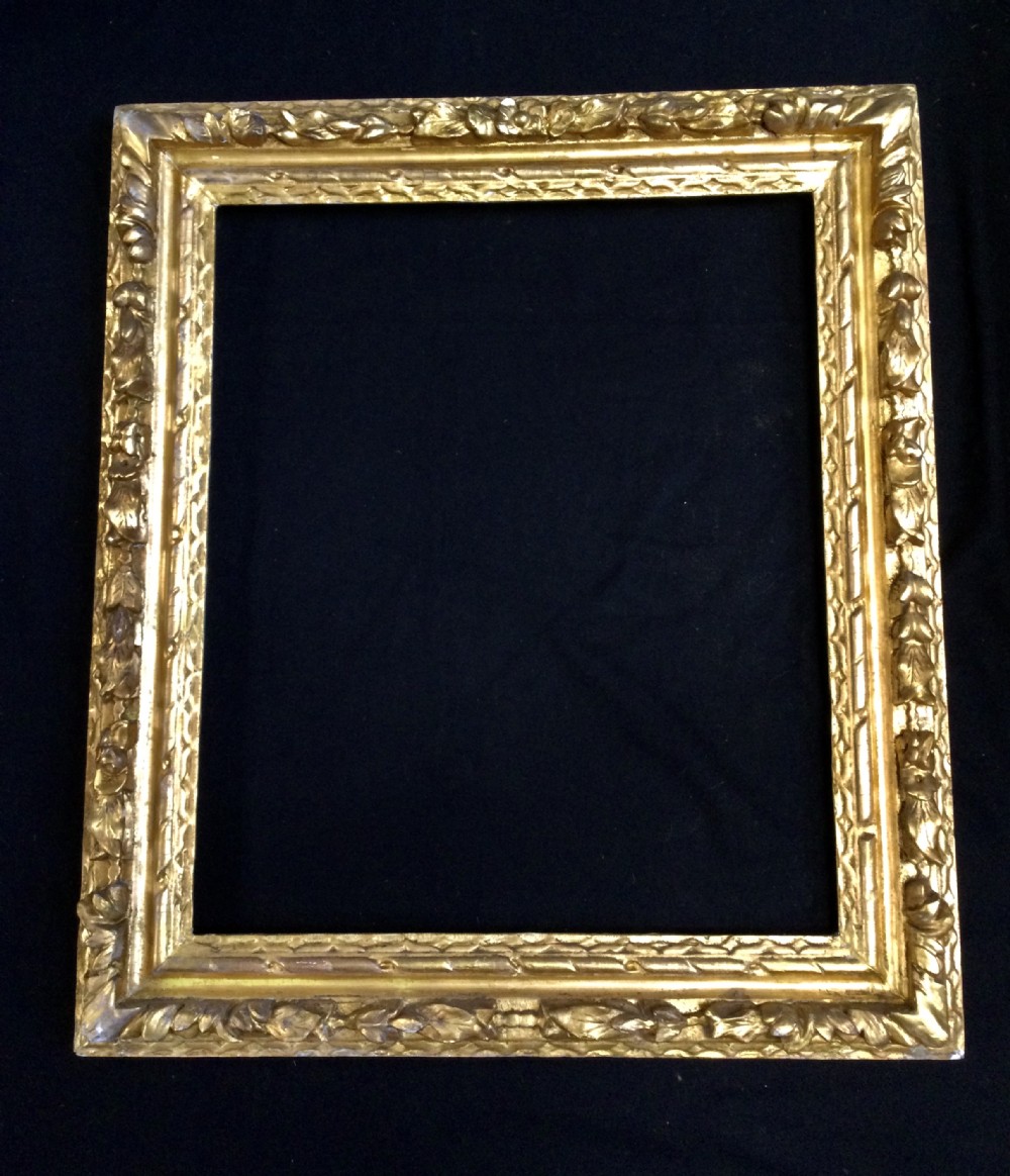 A rectangular antique giltwood picture frame with detailed foliate leaf mouldings and a gold leaf finish against a dark background.