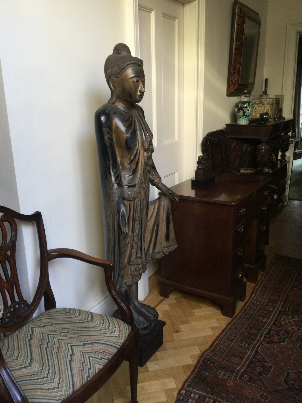 A tall carved wood standing Buddha sculpture with draped flowing robes, dark lacquered surfaces, and intricate glass inlay detailing. View XIV