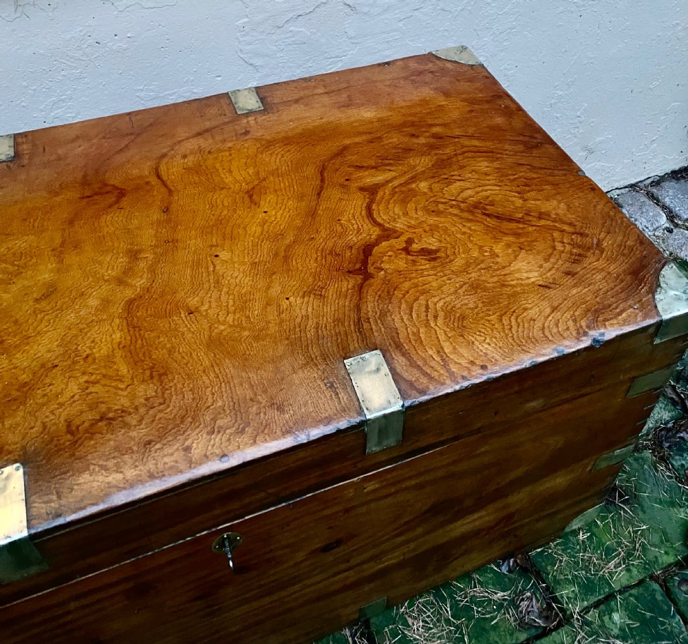 A rectangular warm brown camphor wood trunk featuring brass corner bindings, side carrying handles, and a central keyhole. View VI
