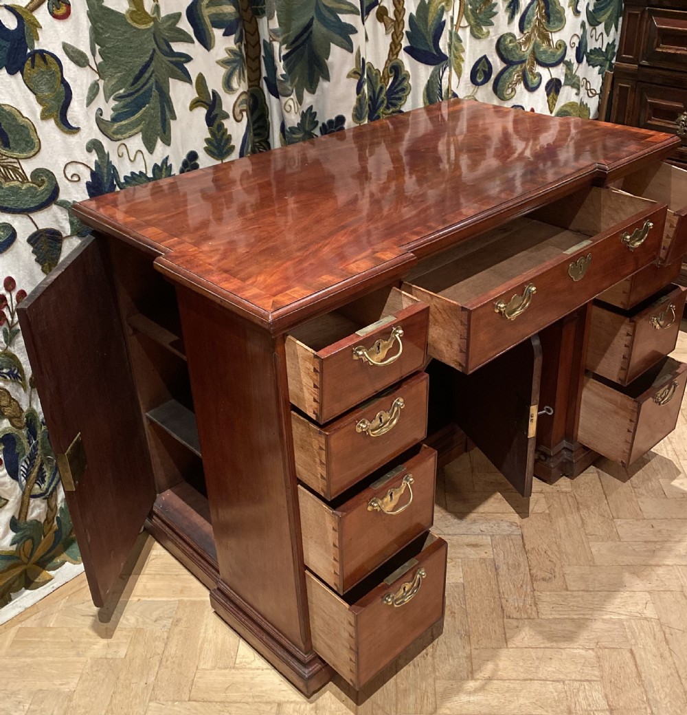 An antique polished mahogany kneehole desk featuring a flat rectangular top, multiple side drawers with brass drop handles, and a central recessed kneehole arch. View II