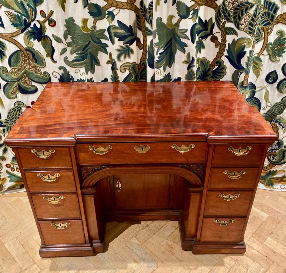 An antique polished mahogany kneehole desk featuring a flat rectangular top, multiple side drawers with brass drop handles, and a central recessed kneehole arch. View III