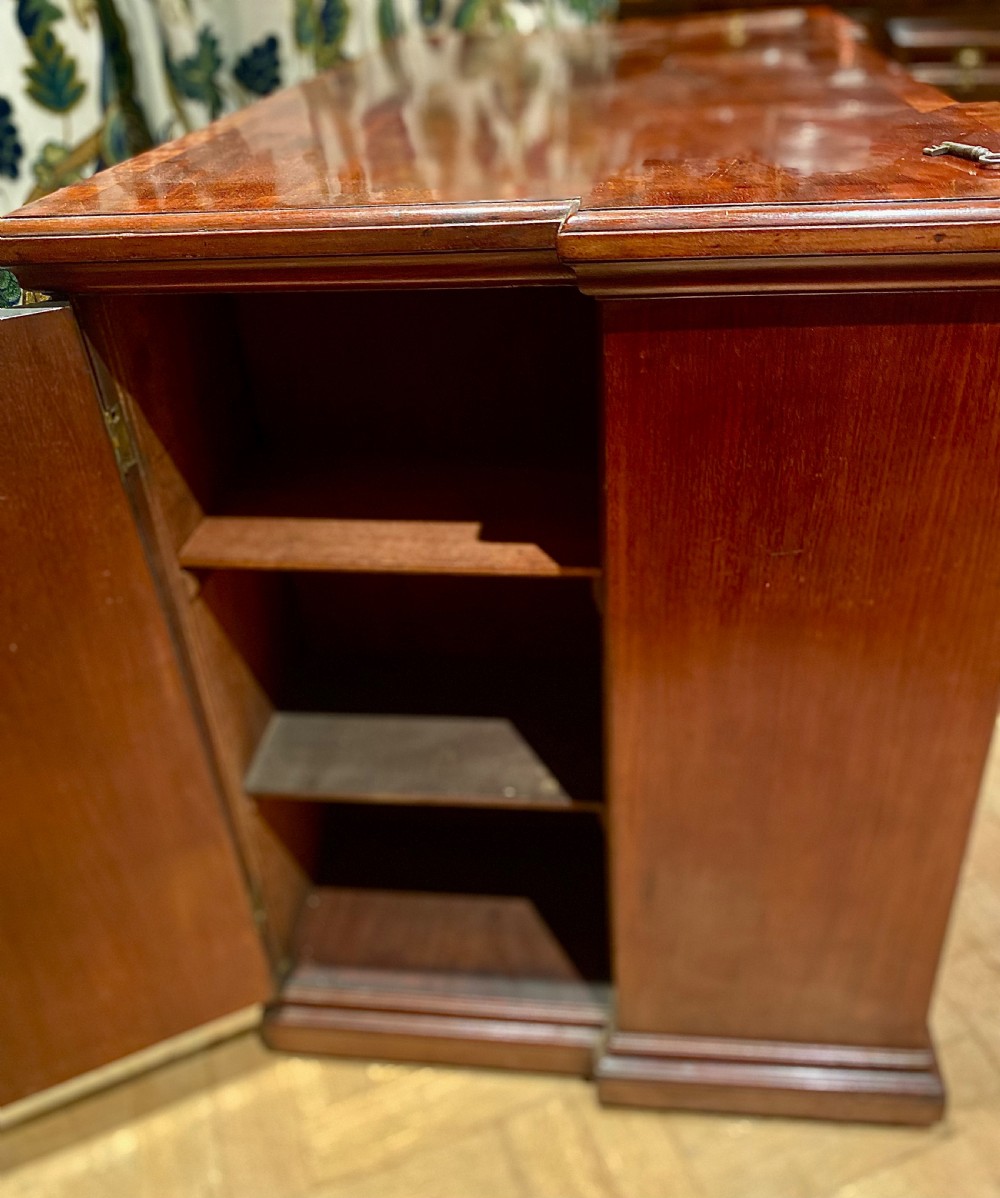 An antique polished mahogany kneehole desk featuring a flat rectangular top, multiple side drawers with brass drop handles, and a central recessed kneehole arch. View VI
