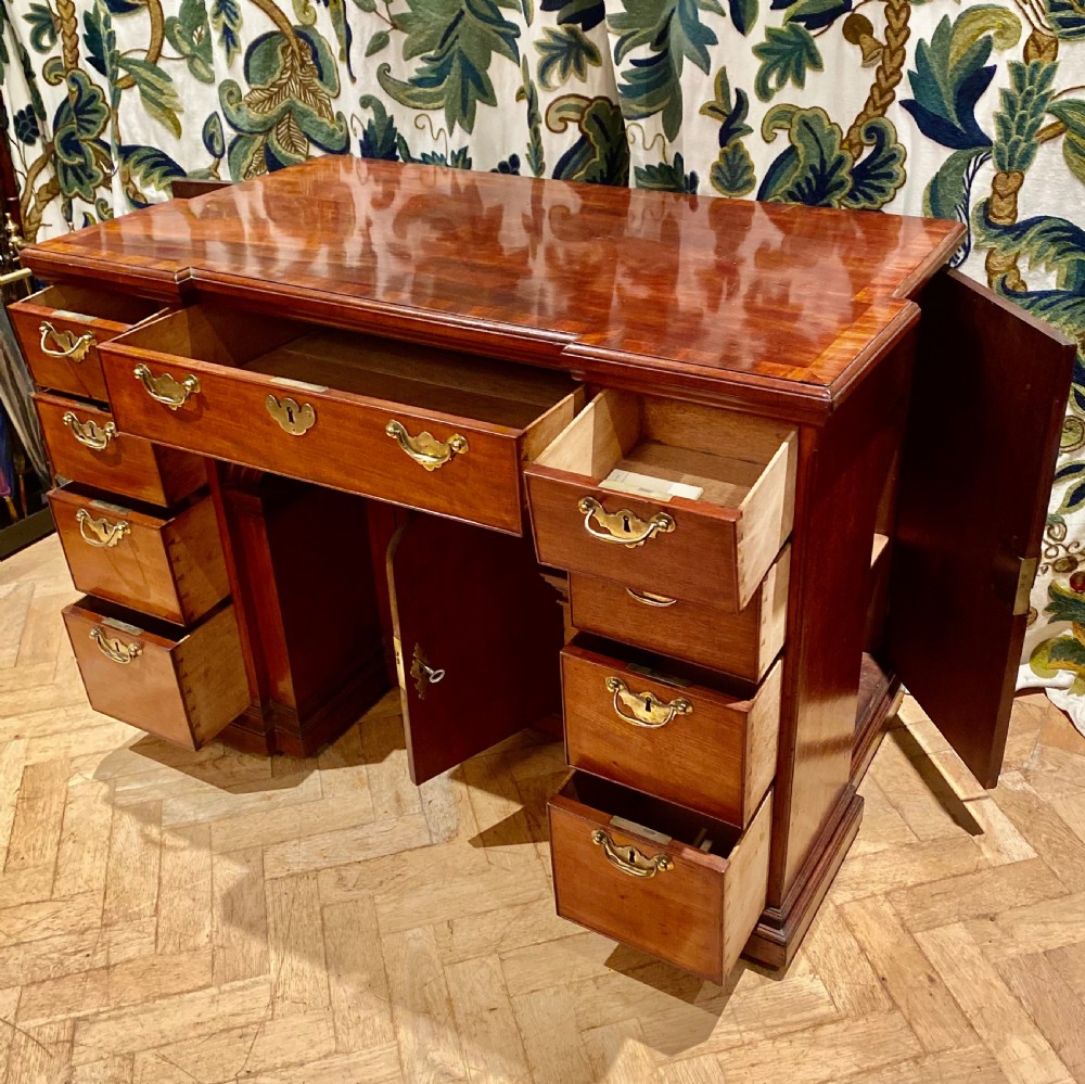 An antique polished mahogany kneehole desk featuring a flat rectangular top, multiple side drawers with brass drop handles, and a central recessed kneehole arch. View VII