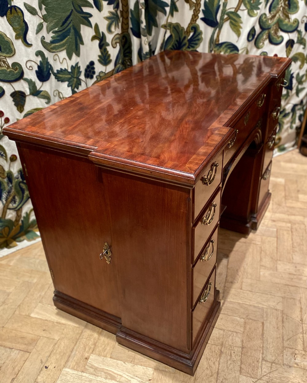 An antique polished mahogany kneehole desk featuring a flat rectangular top, multiple side drawers with brass drop handles, and a central recessed kneehole arch. View VIII