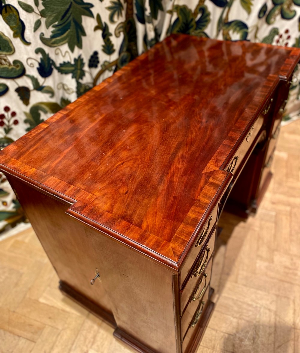 An antique polished mahogany kneehole desk featuring a flat rectangular top, multiple side drawers with brass drop handles, and a central recessed kneehole arch. View IX